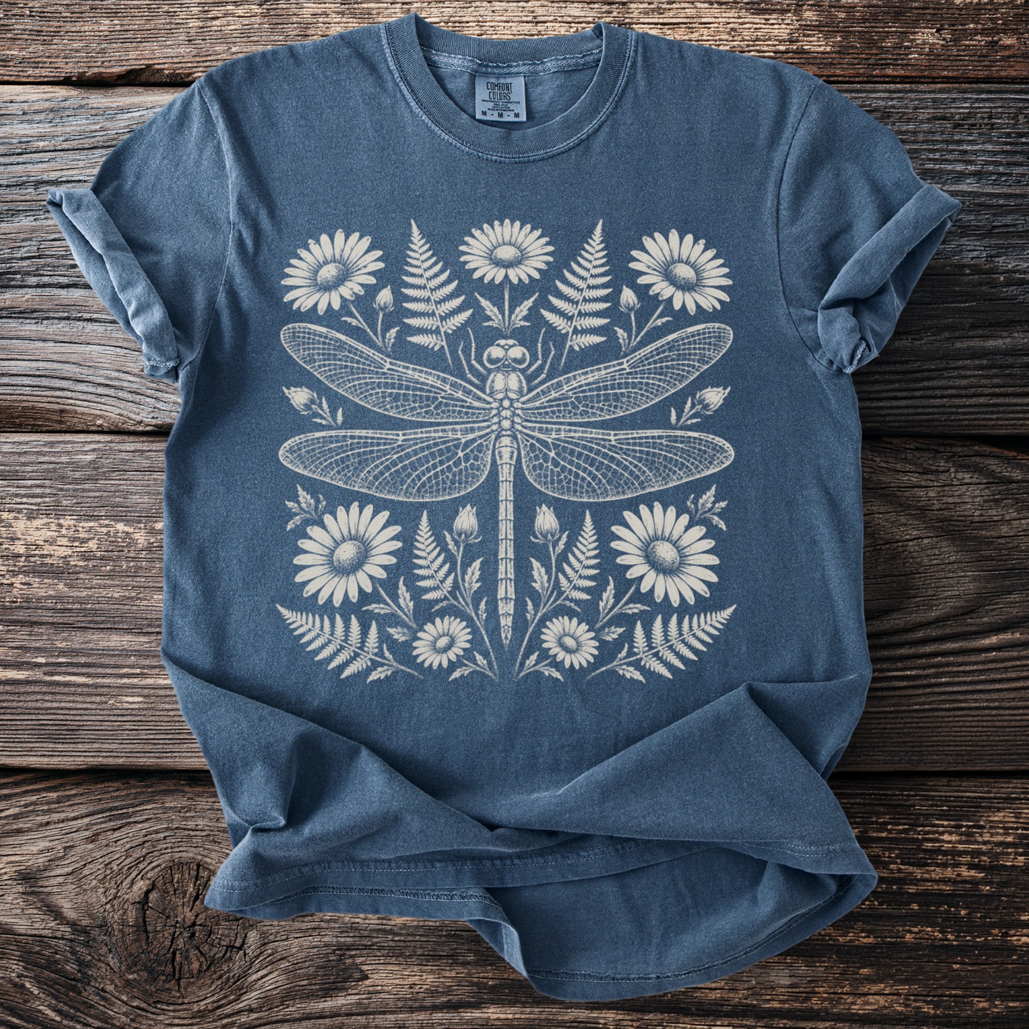 Blue t-shirt with a detailed white illustration of a dragonfly surrounded by flowers and ferns.