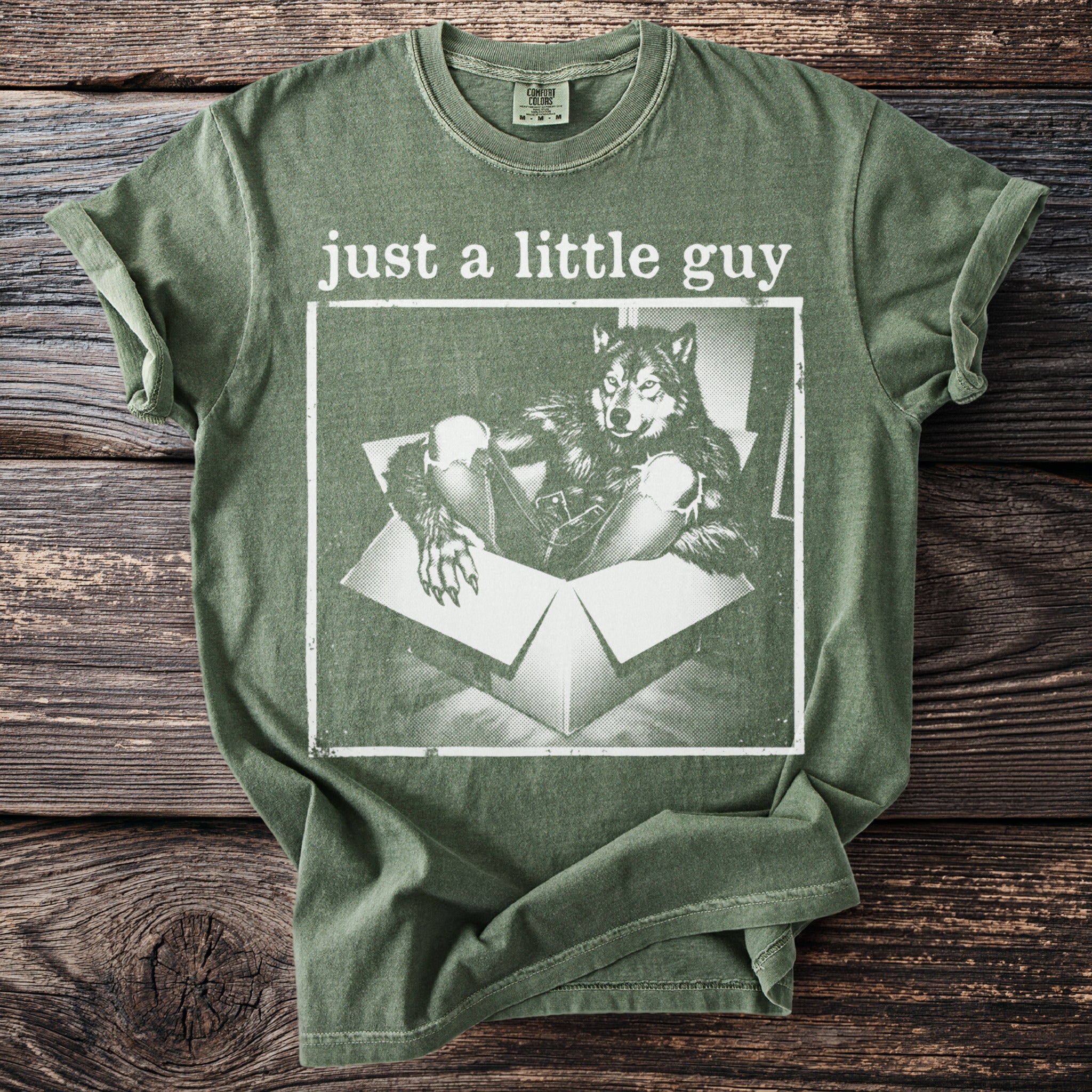 Green t-shirt with a graphic of a wolf in a box and text "just a little guy".