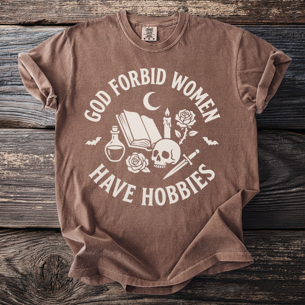 Brown t-shirt with "GOD FORBID WOMEN HAVE HOBBIES" text and occult imagery.