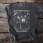 Dark wash t-shirt with "god forbid women have hobbies" and three witches illustration.
