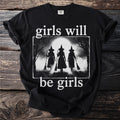 Black t-shirt with "girls will be girls" text and a graphic of three witches with brooms.