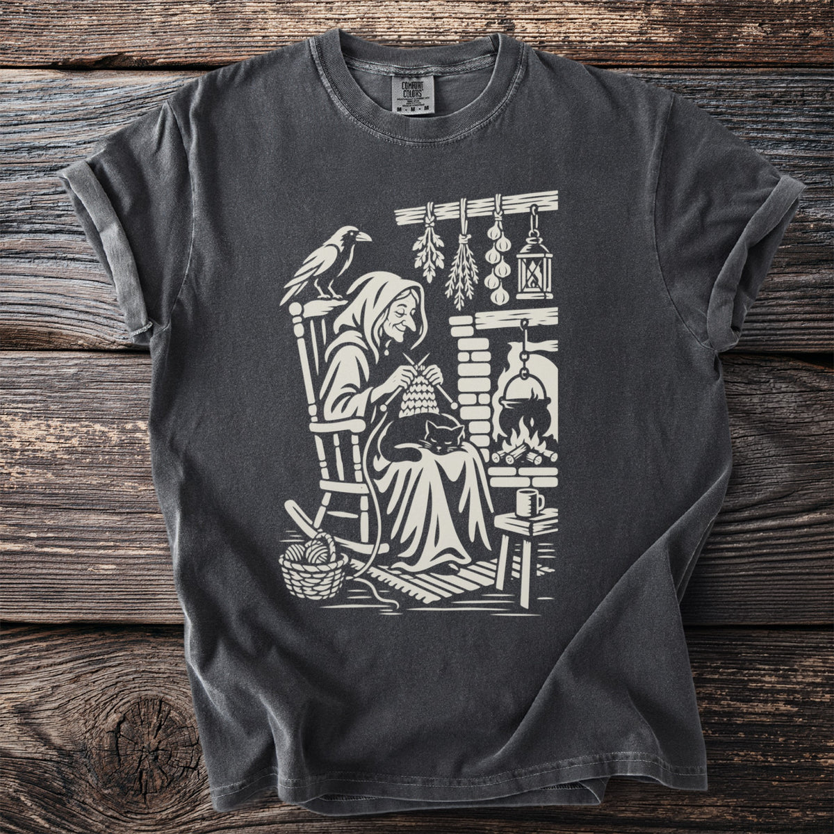 Graphic of witch knitting by fireplace with cat, raven, and herbs.