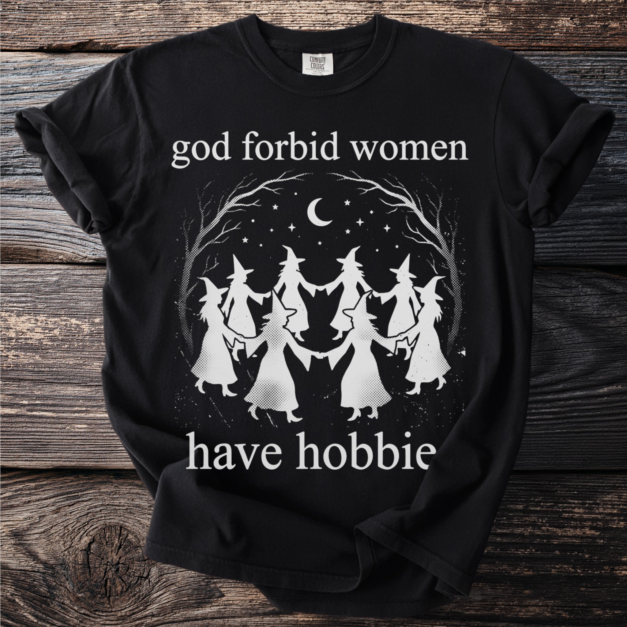 Black t-shirt with white graphic of witches dancing under a moon and stars, reading "god forbid women have hobbie".