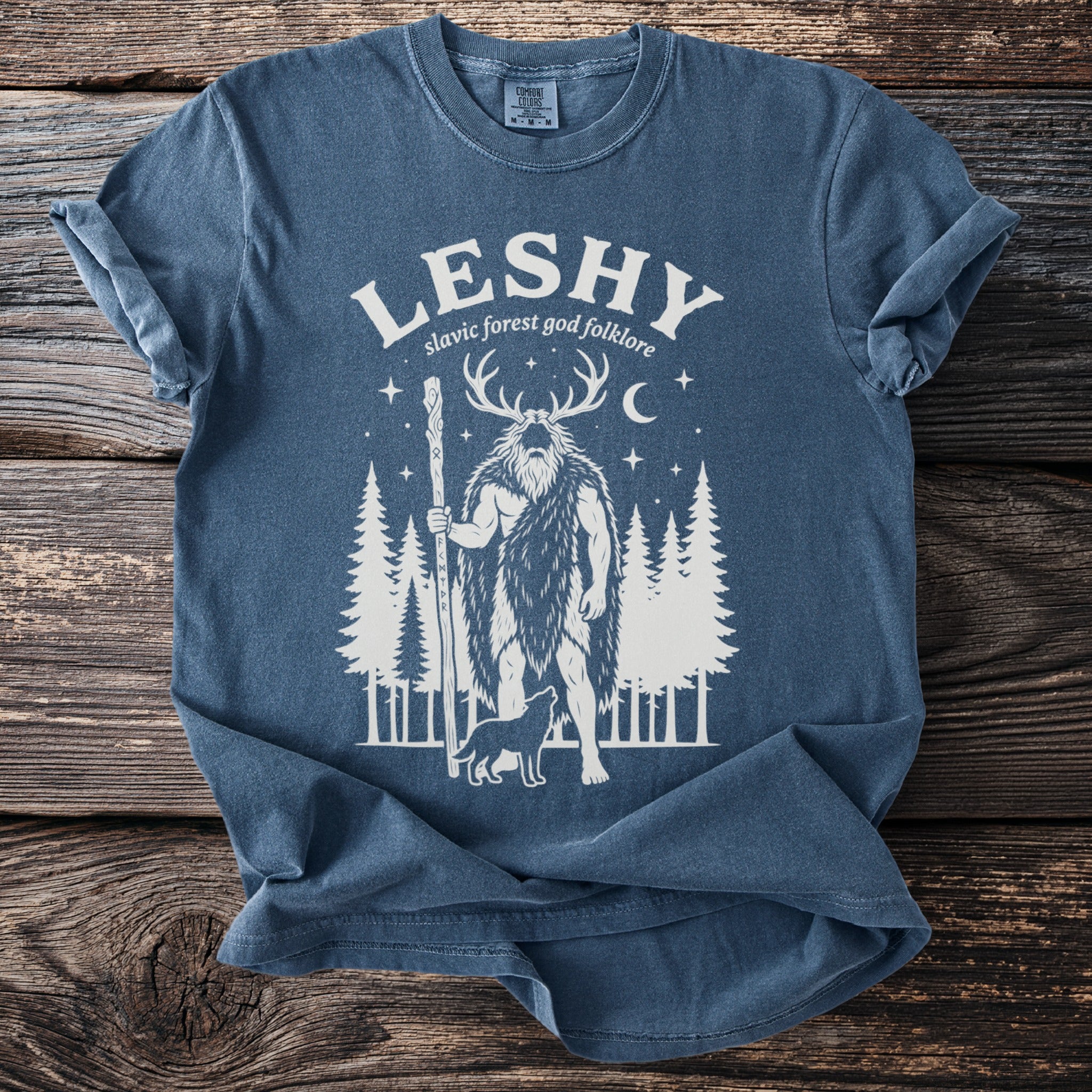 Blue t-shirt with graphic of Leshy, Slavic forest god, folklore, trees, and wolf.