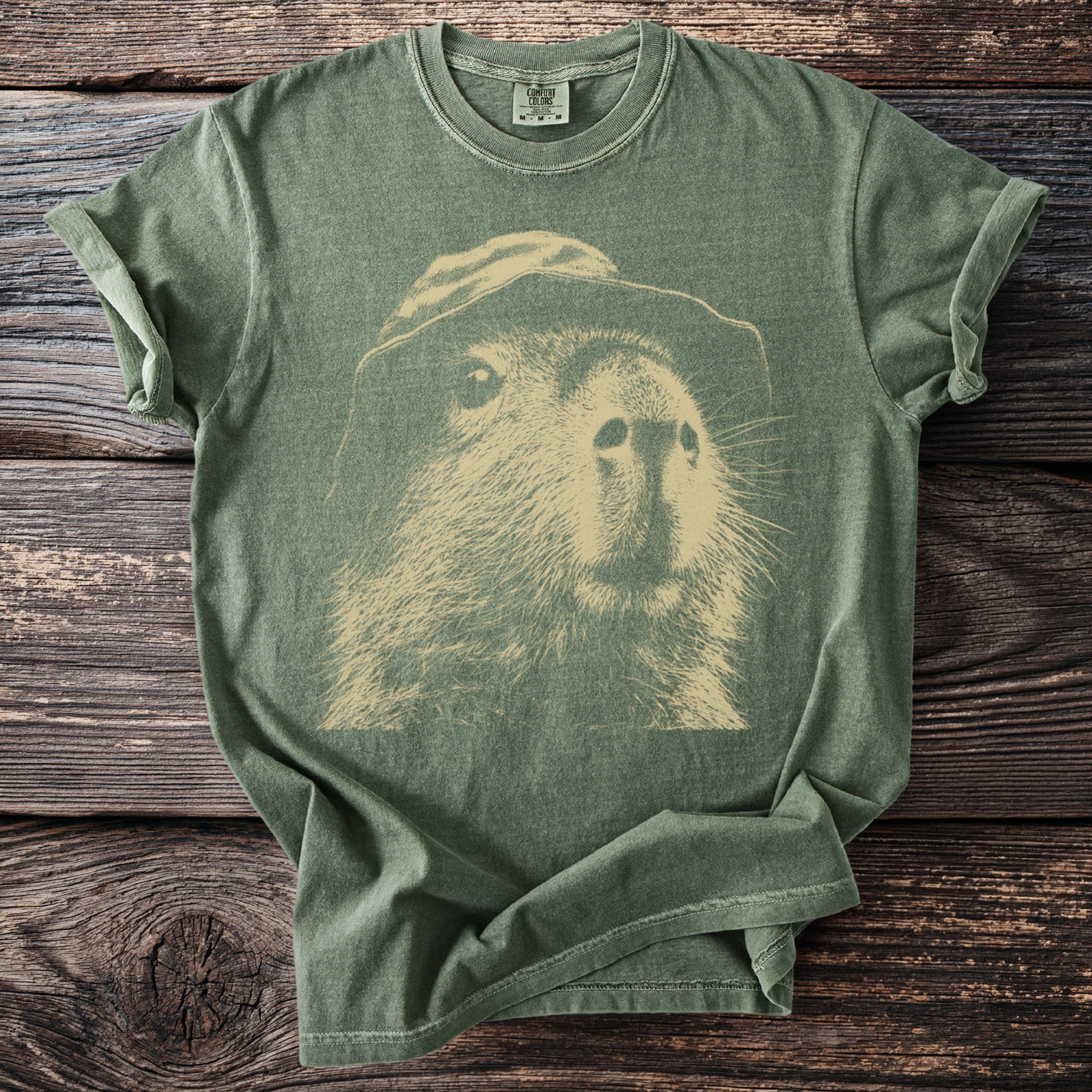 Green t-shirt with a vintage stencil graphic of a capybara wearing a hat.