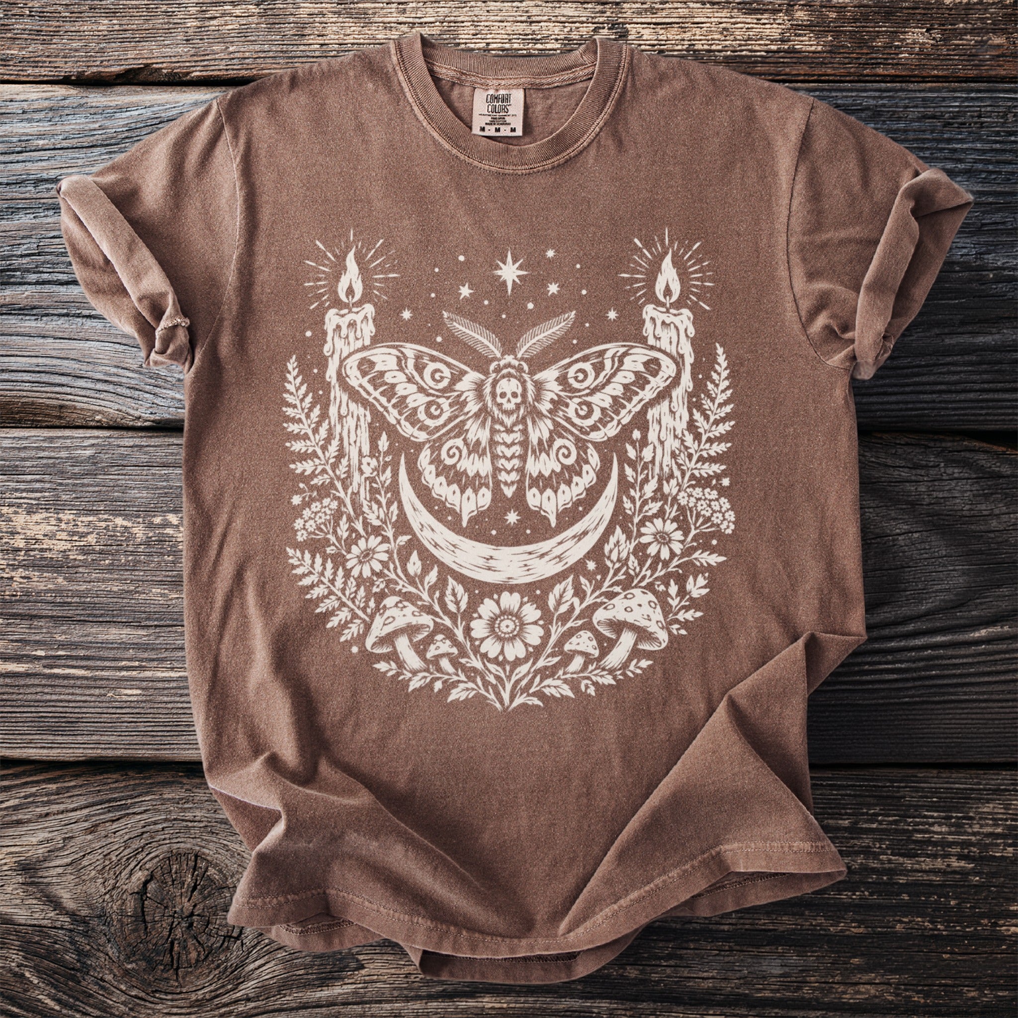 Brown t-shirt with white moth, moon, candles, mushrooms, and stars graphic.