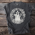 Dark grey t-shirt with white witch, book, herbs, and floral design.