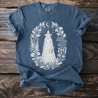 Blue shirt with white witch illustration surrounded by celestial flora and fauna.