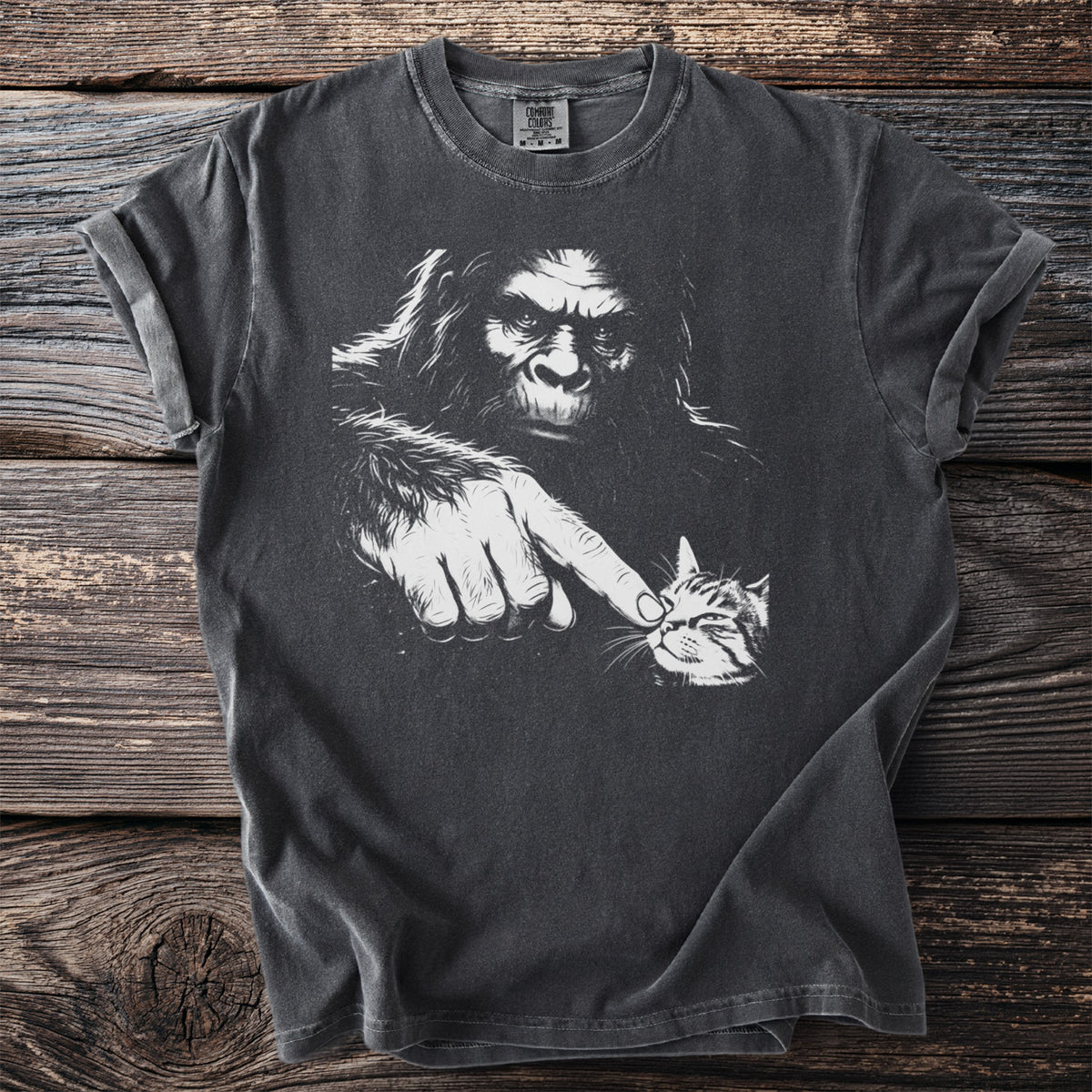 Bigfoot boops a tabby cat on the nose on a charcoal gray t-shirt.