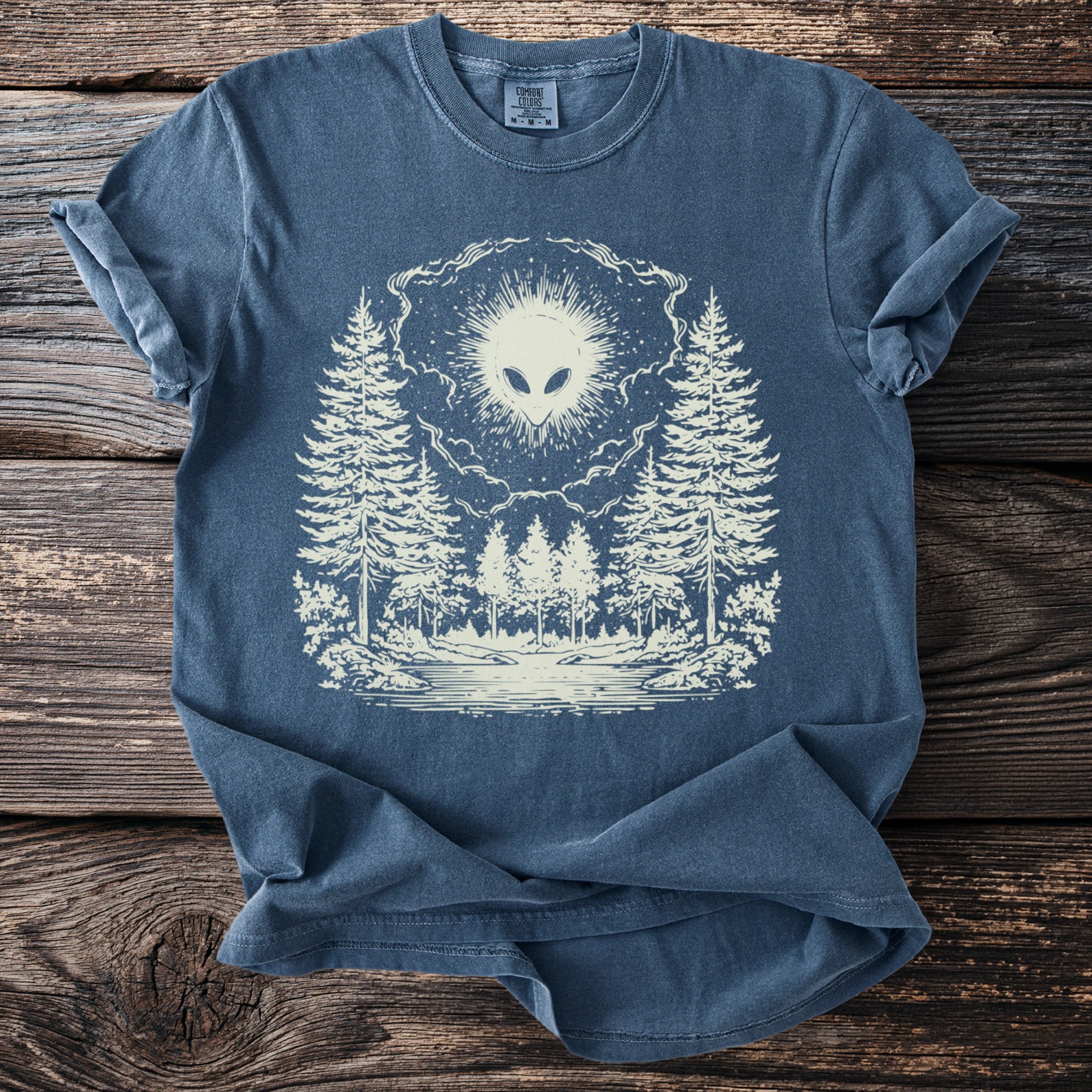 Blue t-shirt with cream graphic of an alien head over a forest scene.