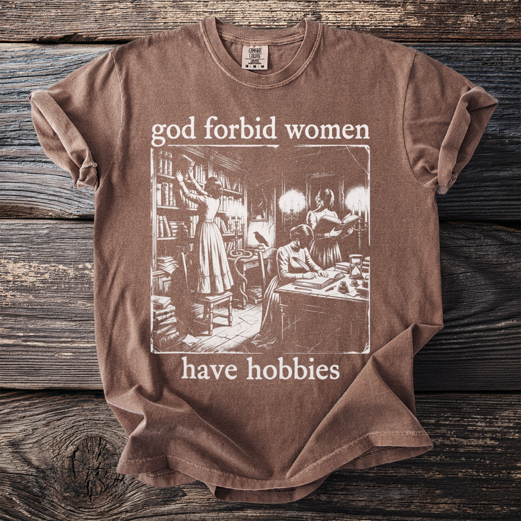 Brown t-shirt with "god forbid women have hobbies" and vintage illustration of women in library.
