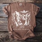 Brown t-shirt with white graphic of figures in cornfield, holding pumpkin and sickle. Text reads "girls will be girls."