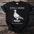 Black t-shirt with a pigeon illustration and the text "STILL HERE Fig. 1: Local Dinosaur."