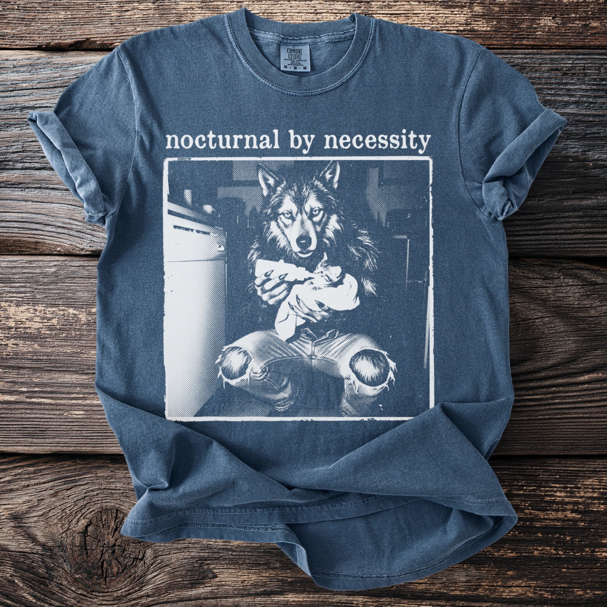 Blue t-shirt with "nocturnal by necessity" and graphic of wolf feeding a kitten.