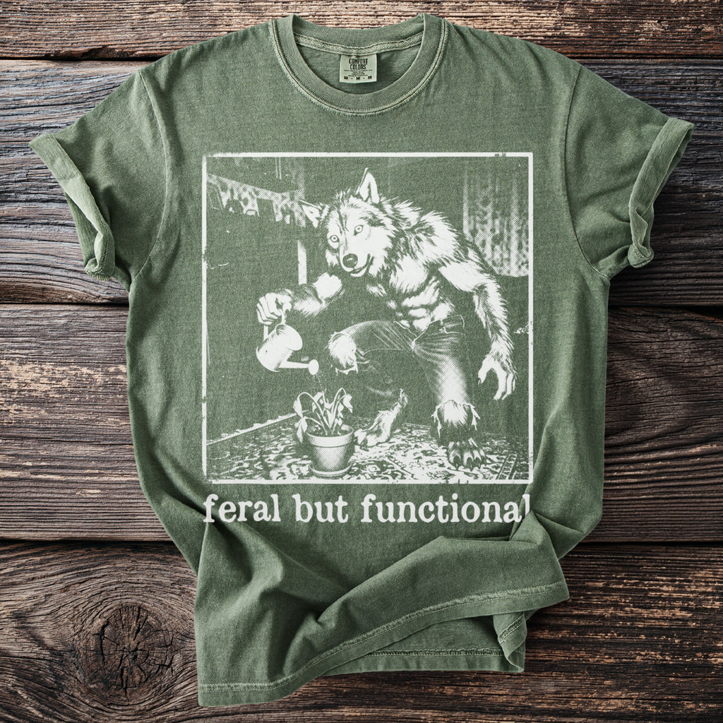 Green t-shirt with a werewolf watering a plant, text "feral but functional".