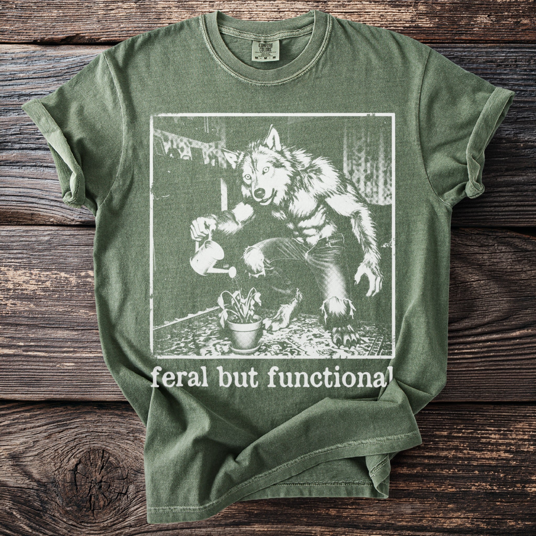 Green t-shirt with a werewolf watering a plant, text "feral but functional".