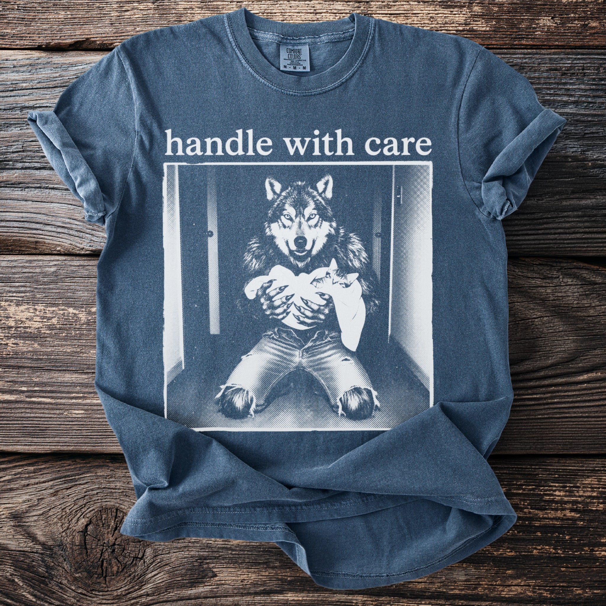 T-shirt graphic of a wolf holding a cat with text "handle with care".