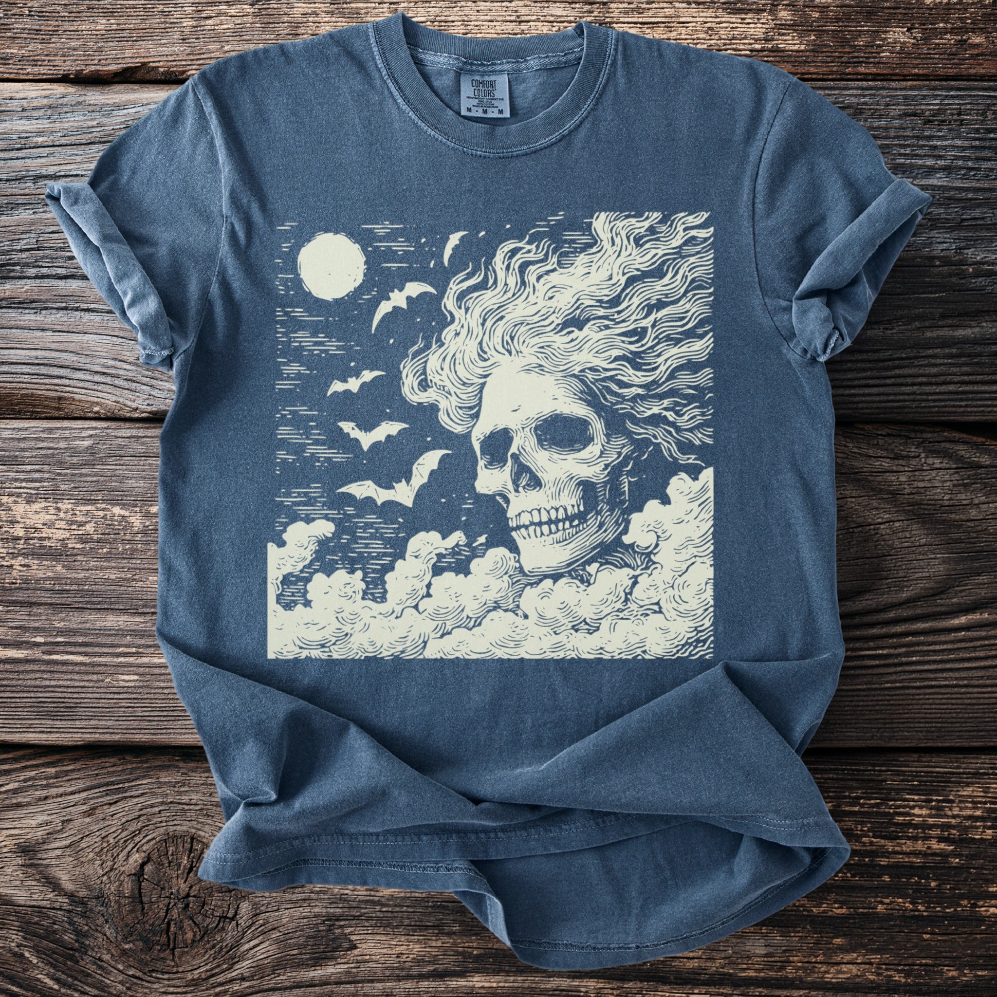 T-shirt with a cream-colored skull, bats, and moon graphic on dark blue fabric.