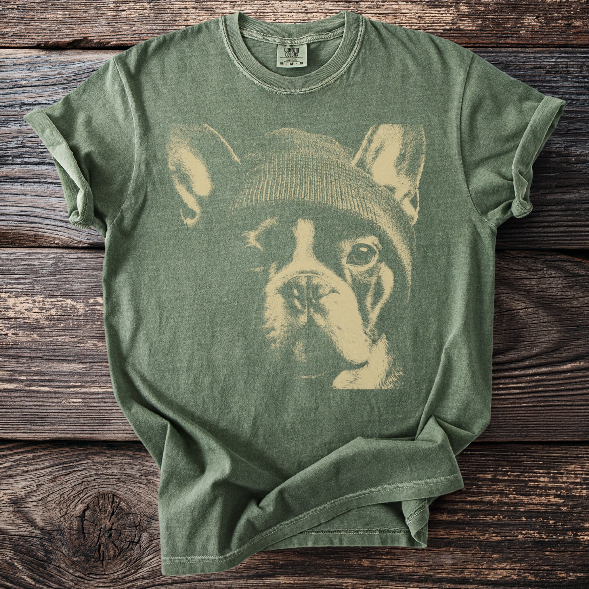 Green t-shirt with a cream graphic of a French bulldog wearing a beanie.