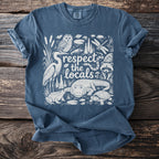 Blue t-shirt with white graphic art of swamp animals and the text "respect the locals".