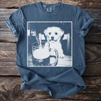 White fluffy dog watches beer being poured into a glass on a t-shirt.