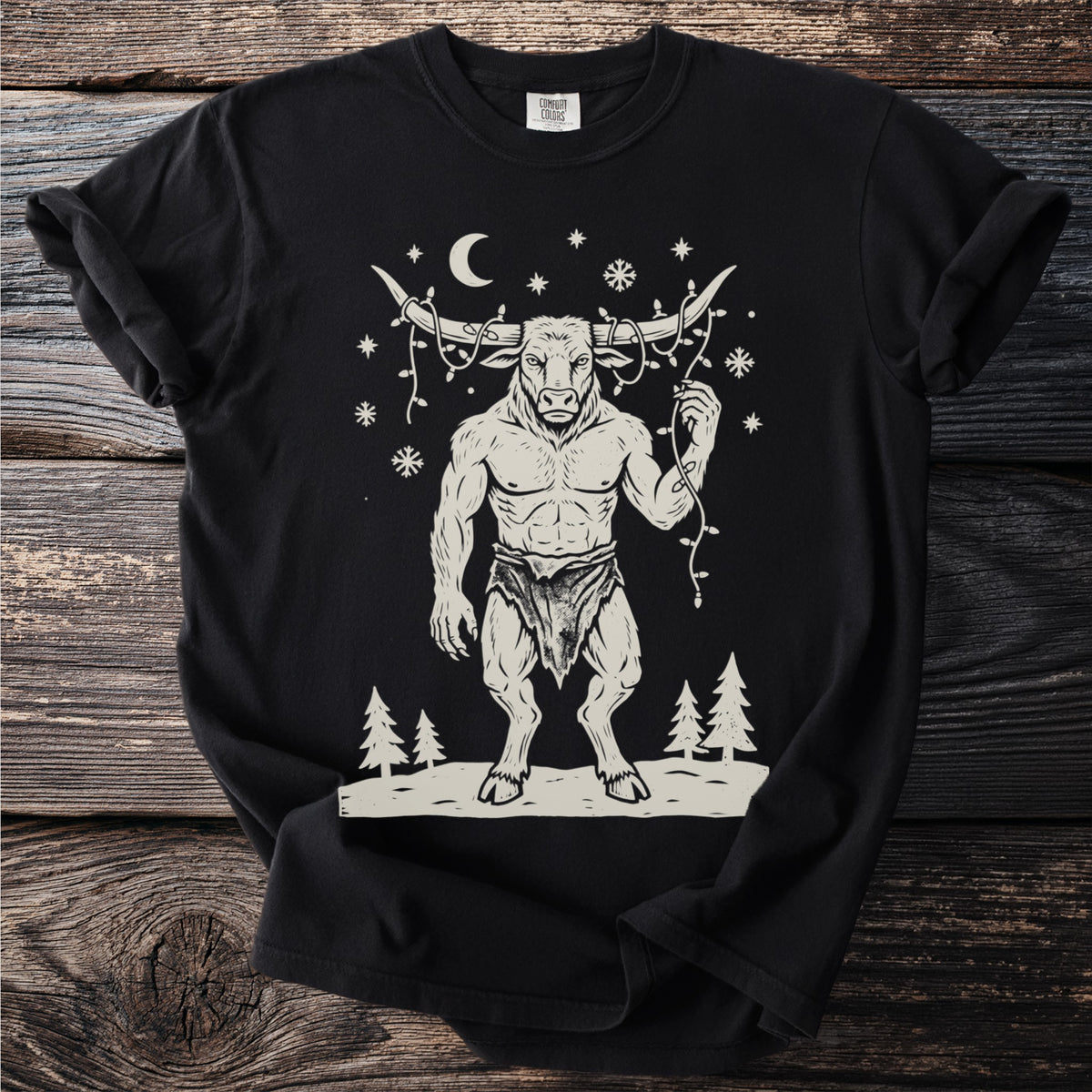 Black t-shirt with a cream folk-cut print: the Minotaur stands in the snow with a string of Christmas lights tangled around his horns.