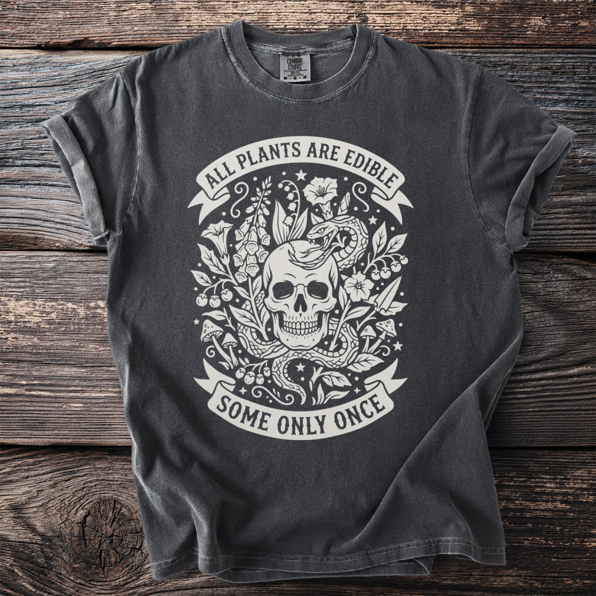 Dark t-shirt with skull, snake, plants, and text "ALL PLANTS ARE EDIBLE SOME ONLY ONCE".