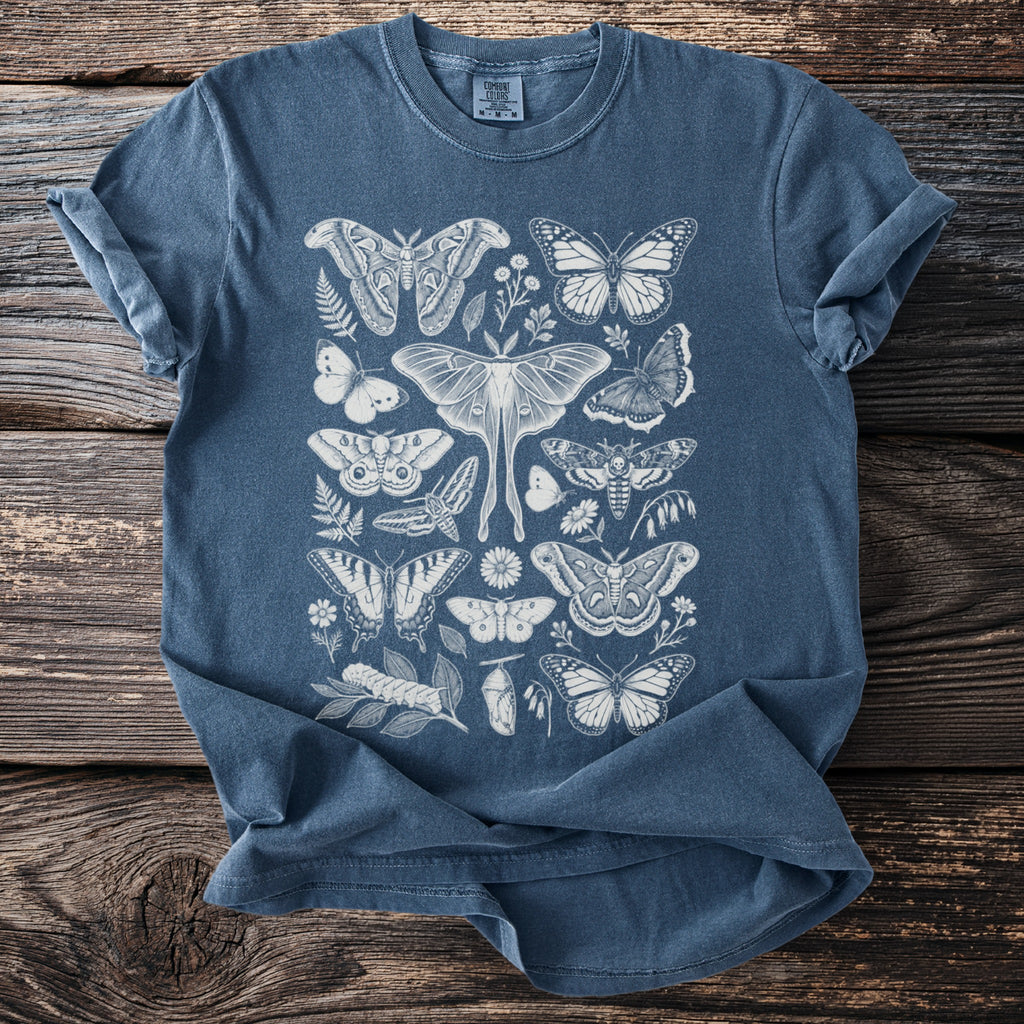 Blue t-shirt with white line art illustration of various moths, butterflies, leaves, and flowers.