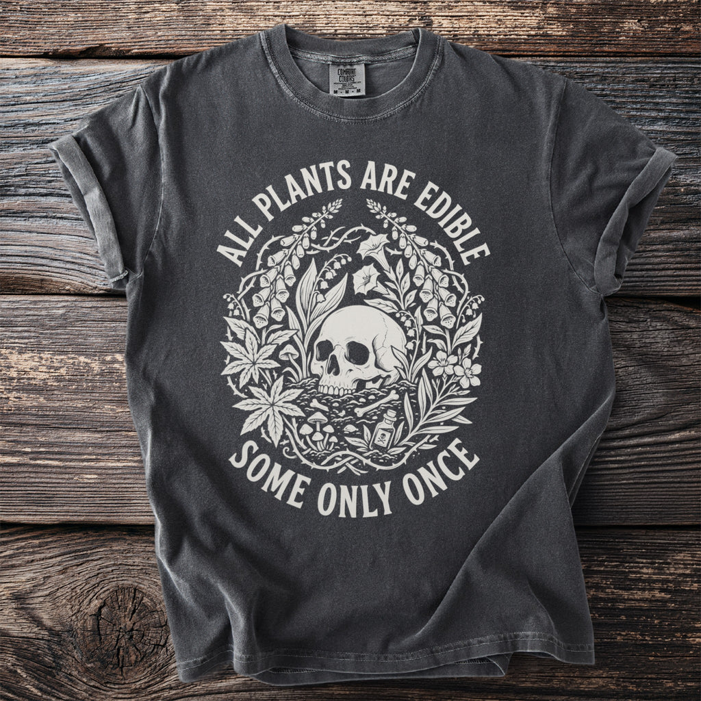 Dark grey t-shirt with a circular graphic of a skull, plants, mushrooms, and the text "ALL PLANTS ARE EDIBLE SOME ONLY ONCE."