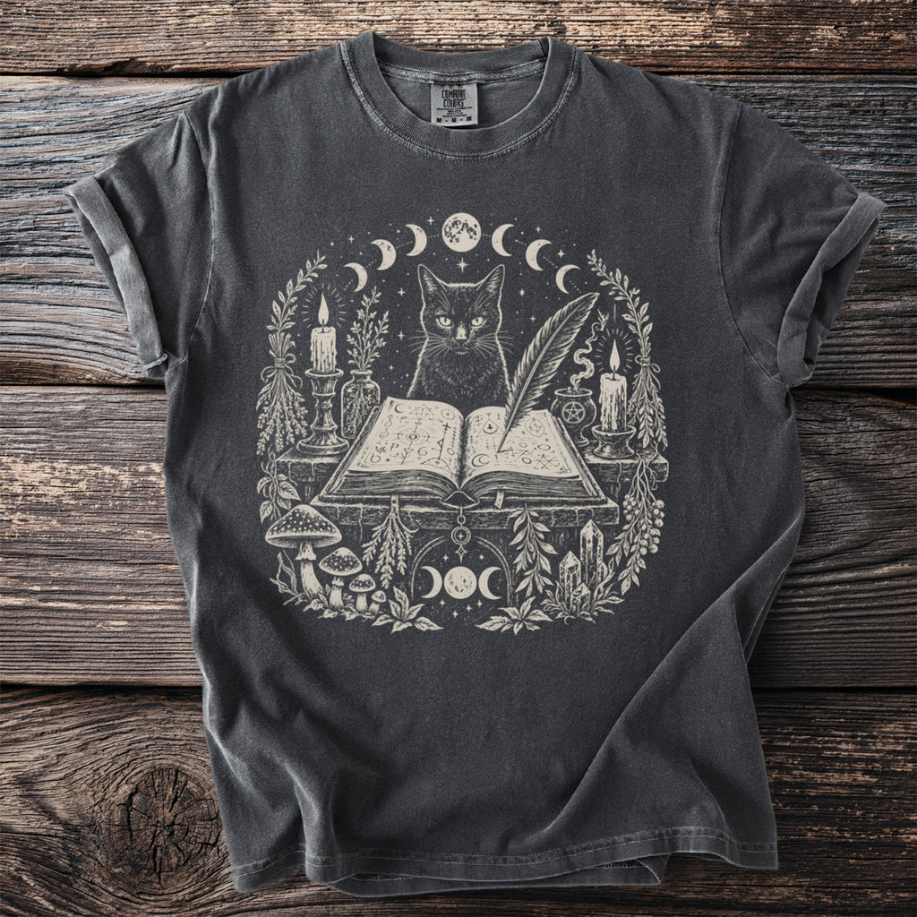 Dark t-shirt with a mystical black cat, open book, candles, and moon phases design.