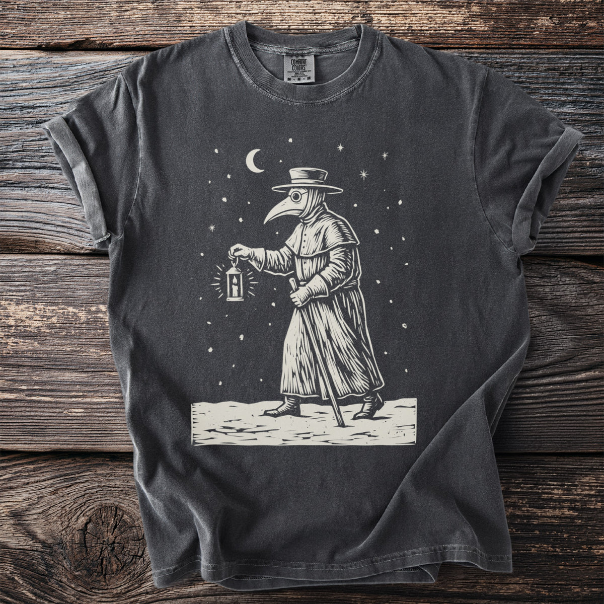 Pepper gray t-shirt with a cream folk-cut print: a plague doctor in beaked mask, hat and long coat walks through falling snow with a lantern.