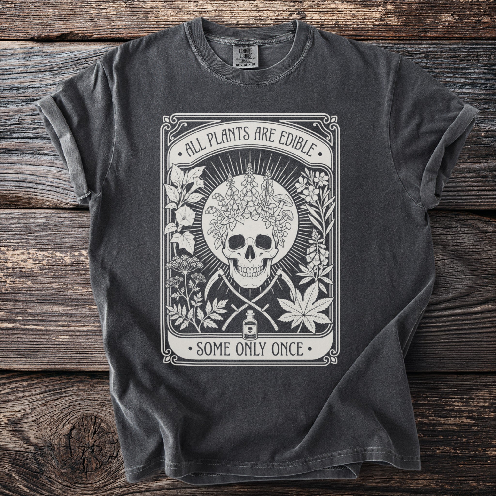Dark grey t-shirt with a skull, plants, and the text "ALL PLANTS ARE EDIBLE SOME ONLY ONCE".