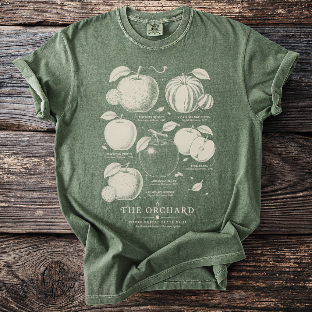 Green t-shirt with vintage orchard illustrations labeled Roxbury Russet, Cox's Orange Pippin, and Pink Pearl.