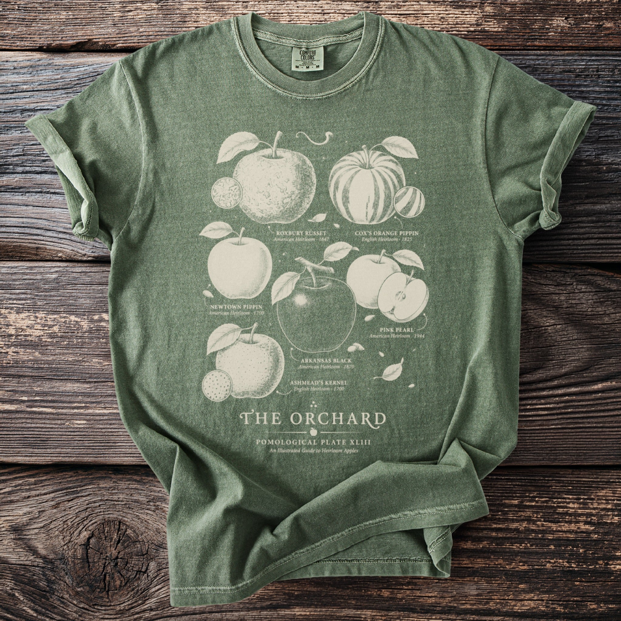 Green t-shirt with vintage orchard illustrations labeled Roxbury Russet, Cox's Orange Pippin, and Pink Pearl.