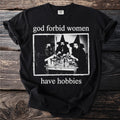 Black t-shirt with text "god forbid women have hobbies" and a B&W image of witches.