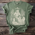 Green t-shirt with a cream design of a woman in a floral crown with two cats and celestial elements.