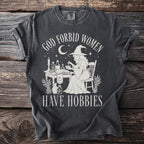 Dark gray t-shirt with "God Forbid Women Have Hobbies" text and witch graphic.