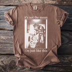 Brown t-shirt with a graphic of a werewolf doing laundry and text "it's not the moon i'm just like this".