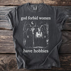 Dark t-shirt with a graphic of three witches and the text "god forbid women have hobbies".