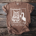 Brown t-shirt with graphic of a raccoon in a cage holding a spoon and a goose outside. Text says "got too silly".