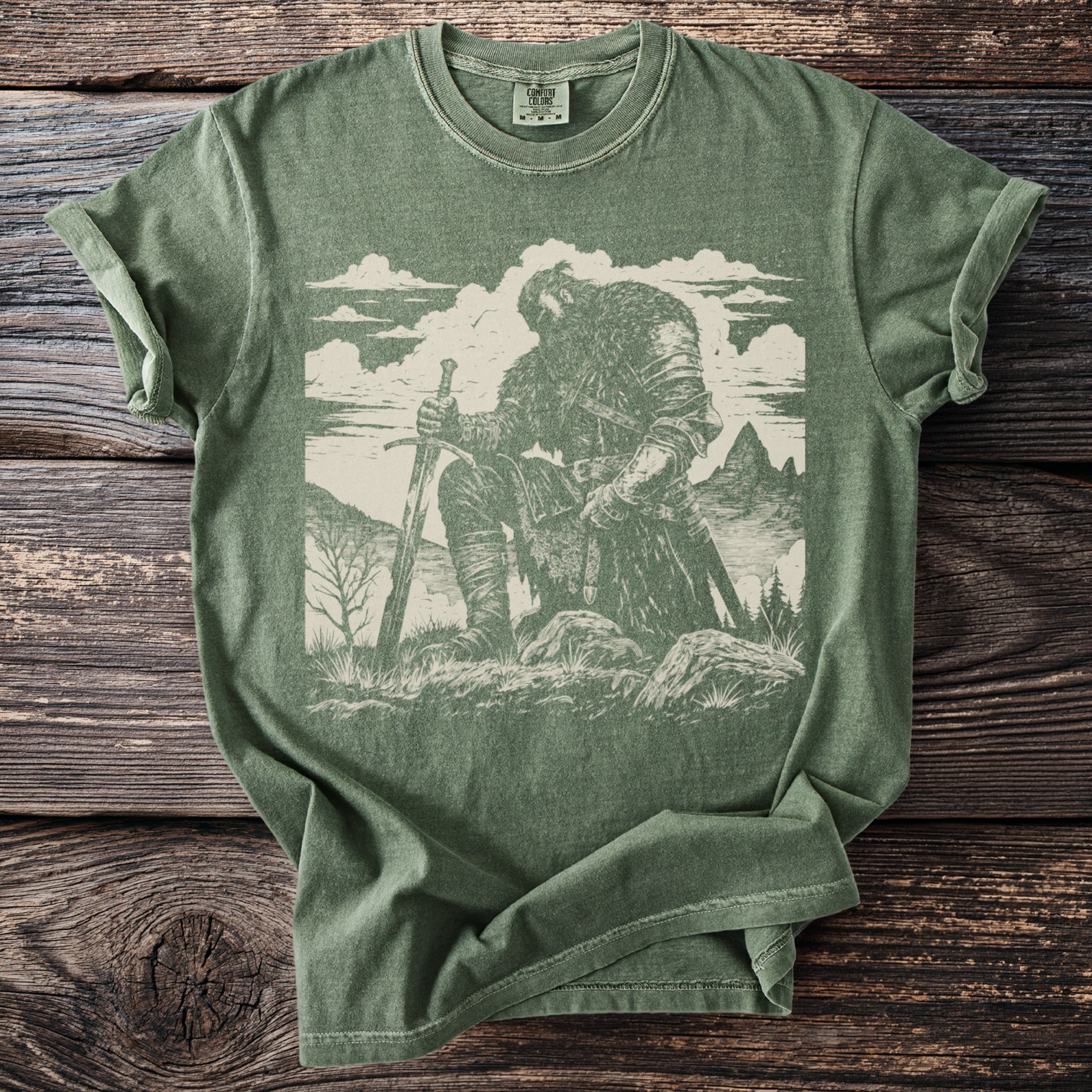 Green t-shirt with a sketched warrior kneeling with a sword, mountains and clouds.