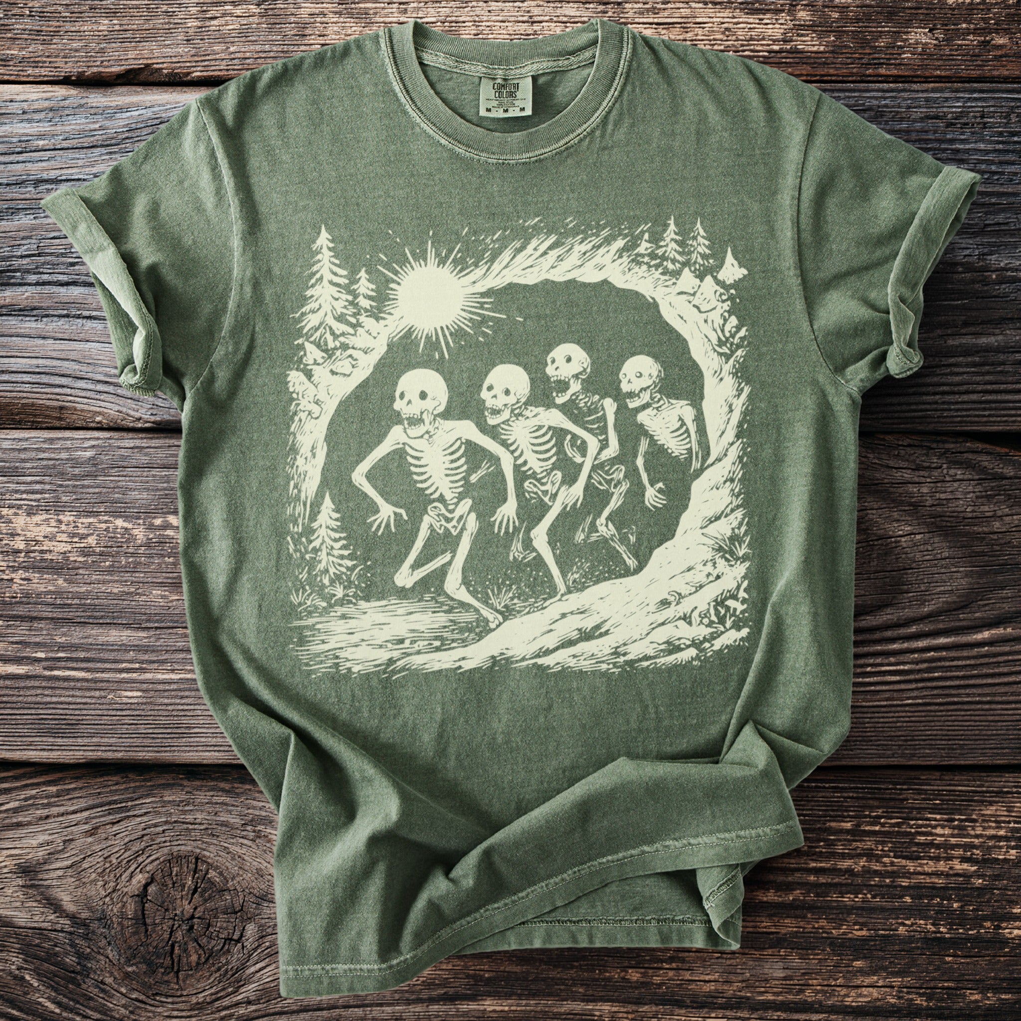 Green Comfort Colors t-shirt with cream-colored graphic of four skeletons running through a forest scene.
