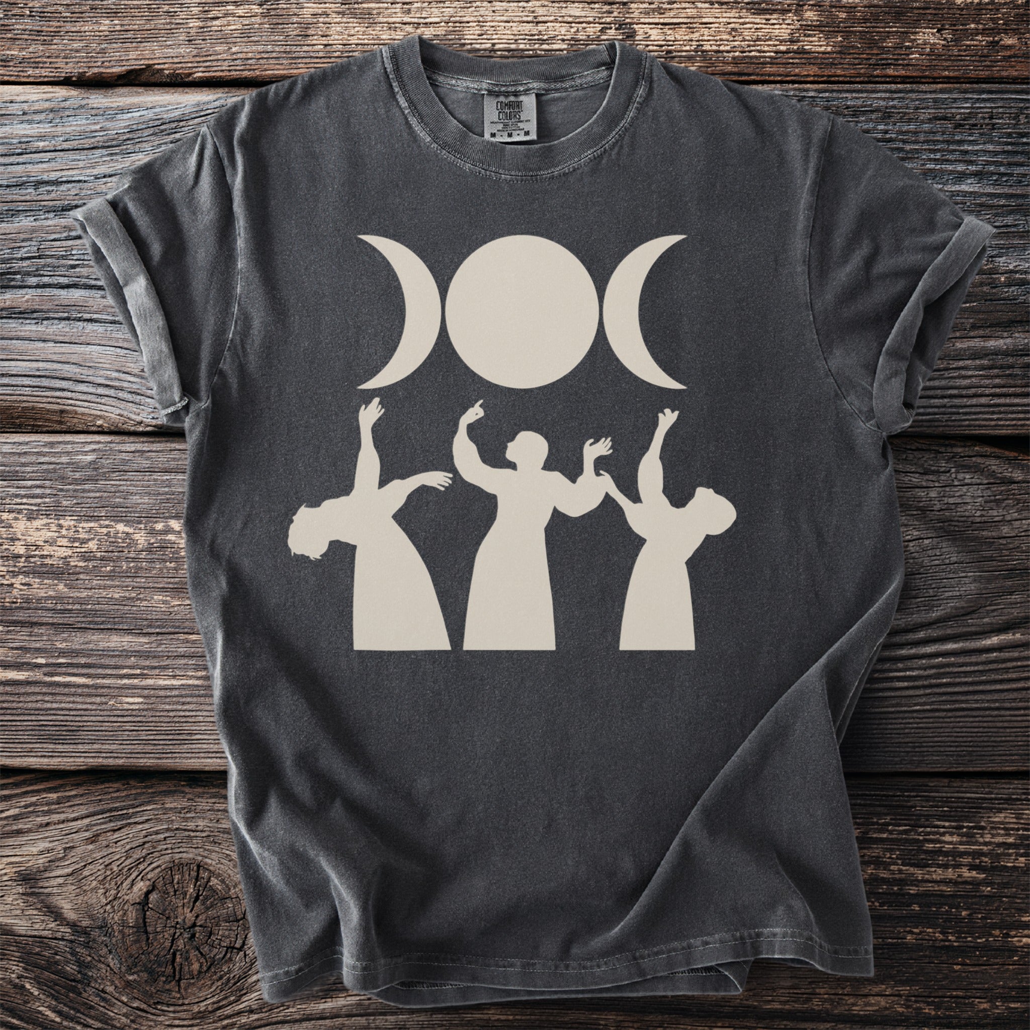 Dark t-shirt with a triple moon goddess symbol and dancing figures.