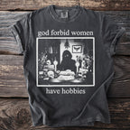 Black t-shirt with text "god forbid women have hobbies" and graphic of person at desk.