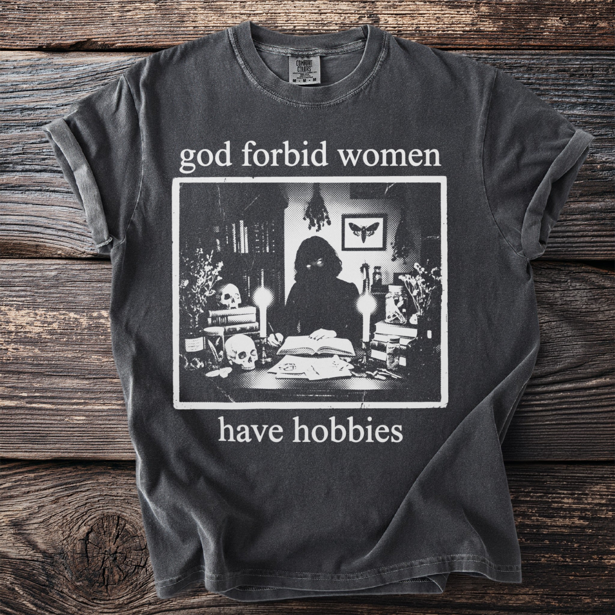 Black t-shirt with text "god forbid women have hobbies" and graphic of person at desk.