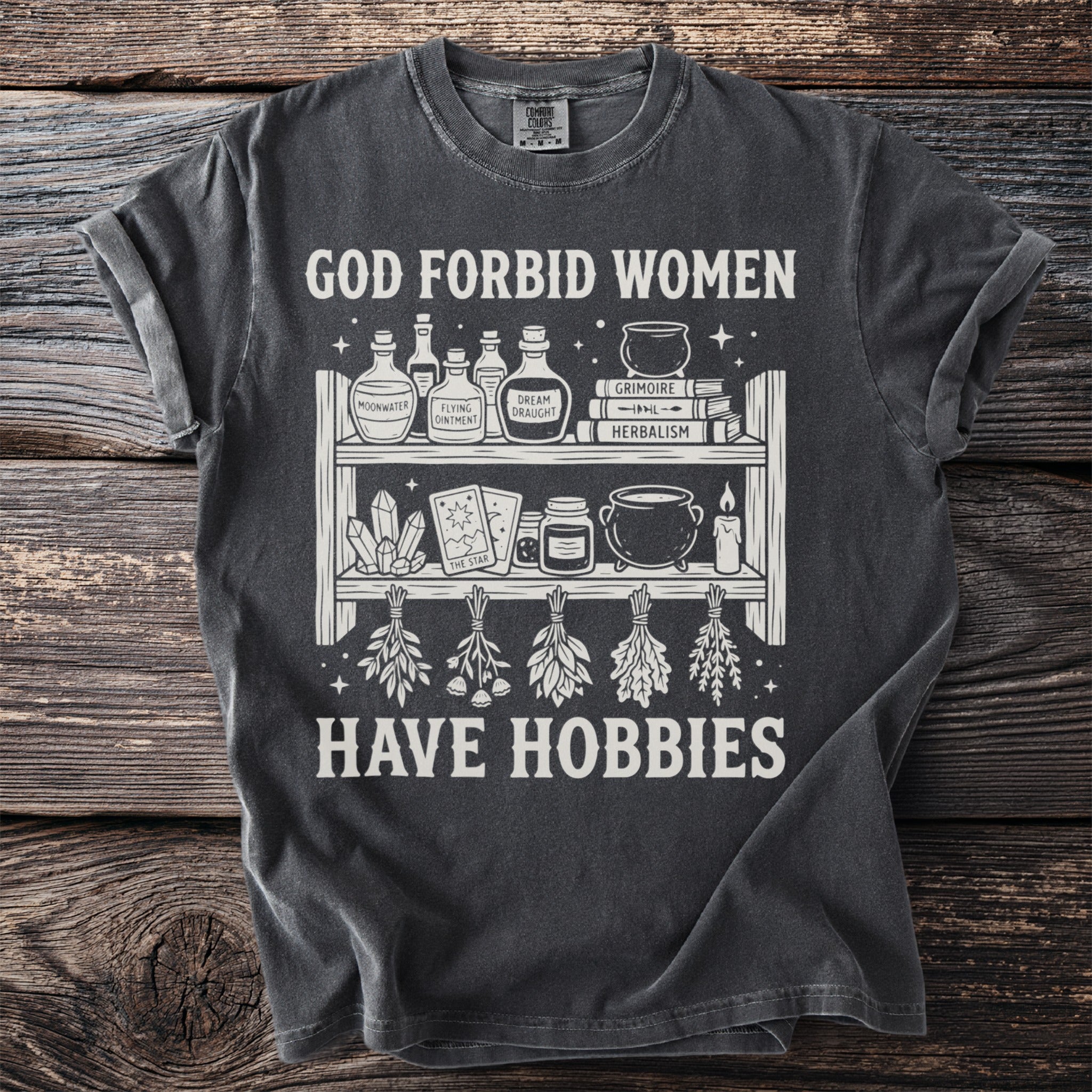 Dark grey t-shirt with "GOD FORBID WOMEN HAVE HOBBIES" and witchy graphics.
