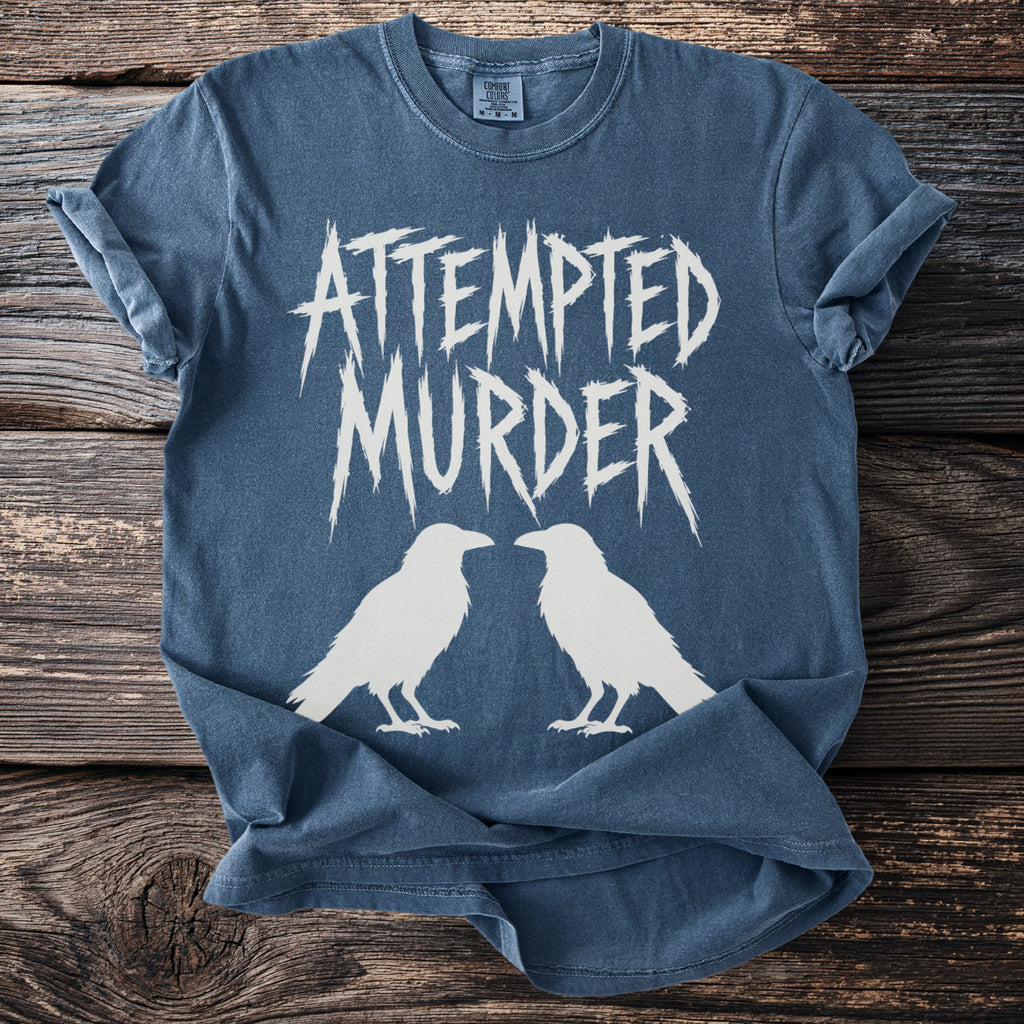 Blue t-shirt with white text "ATTEMPTED MURDER" and two white ravens.