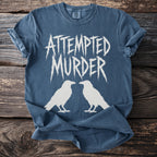 Blue t-shirt with white text "ATTEMPTED MURDER" and two white ravens.