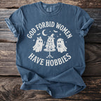 T-shirt with white text "GOD FORBID WOMEN HAVE HOBBIES" and ghost graphics.