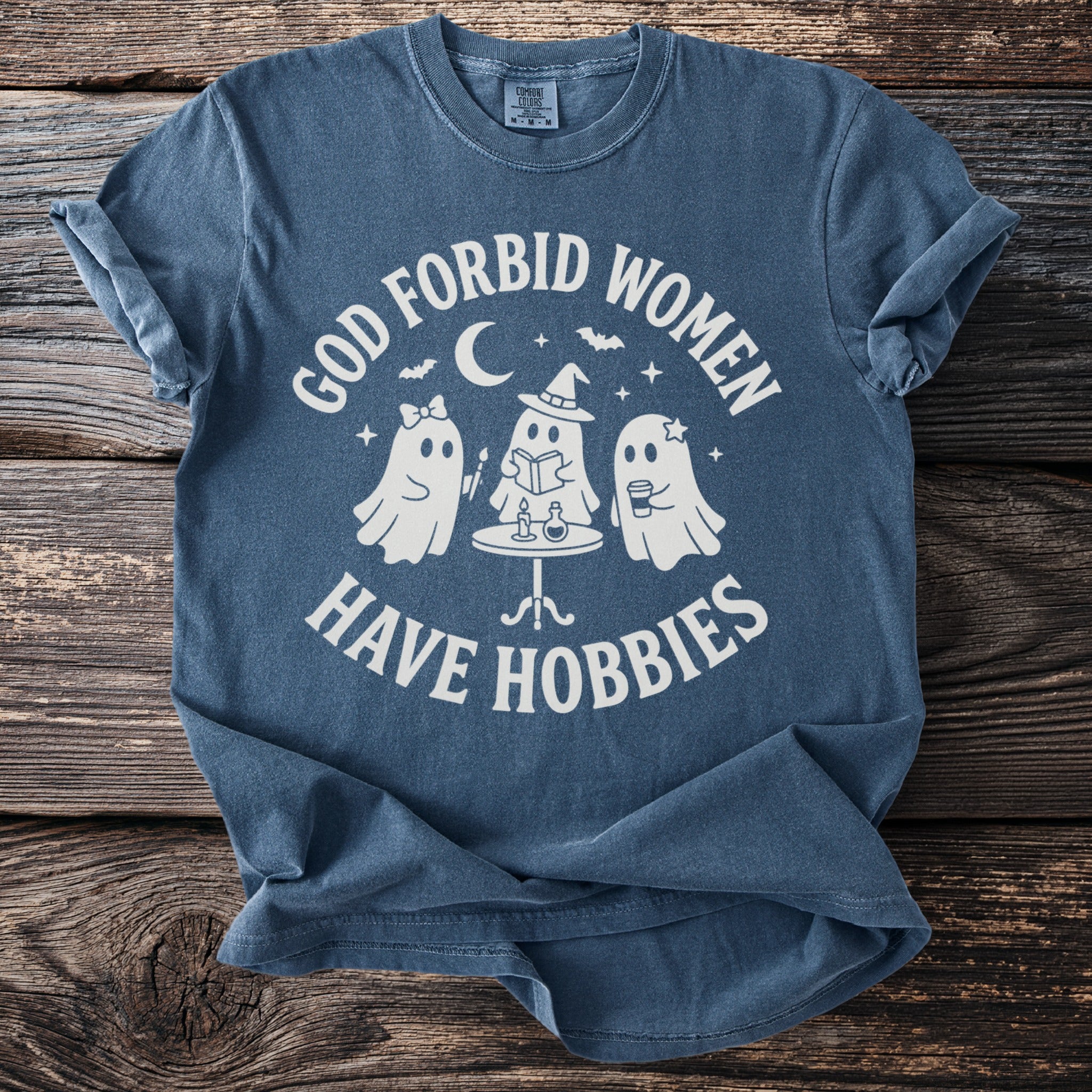 T-shirt with white text "GOD FORBID WOMEN HAVE HOBBIES" and ghost graphics.